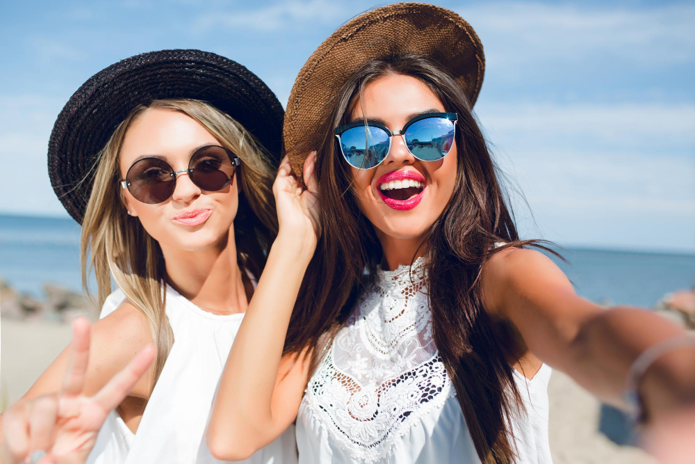 close-up-selfie-portrait-two-attractive-brunette-blonde-girls-with-long-hair-standing-beach-they-wear-hats-sunglasses-white-dresses-they-are-smiling-camera